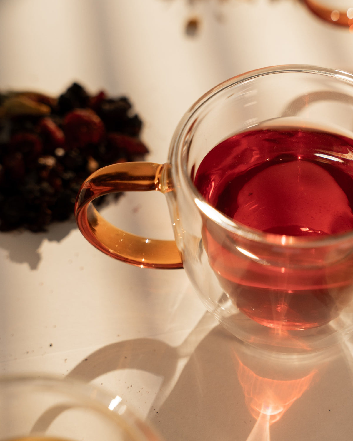 Gather brewed deep berry red in a clear double-wall glass cup, beside the dried blend
