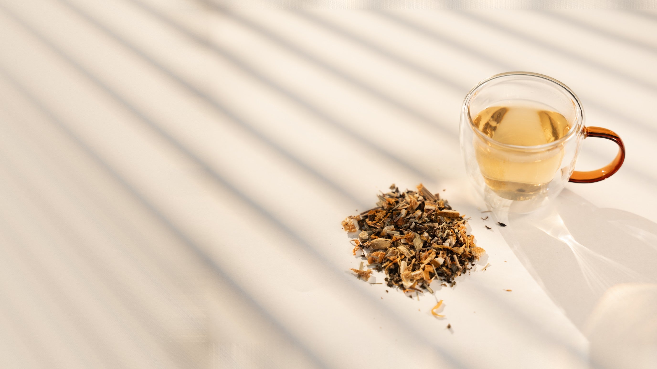 A cup of brewed Daybreak in an amber-handled glass beside a pile of the loose blend, in slatted sunlight