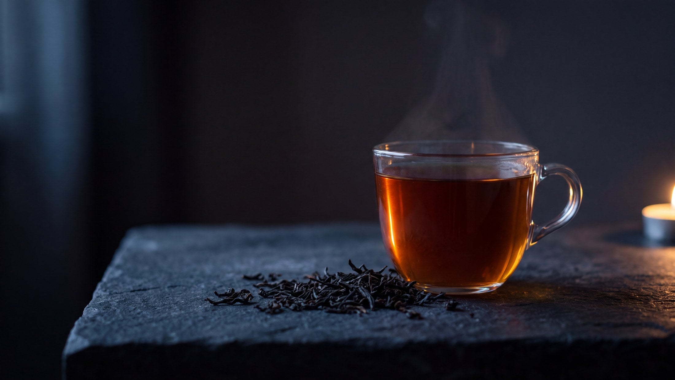 A glass of amber Dusk tea glowing in a dark evening beside loose black tea leaves