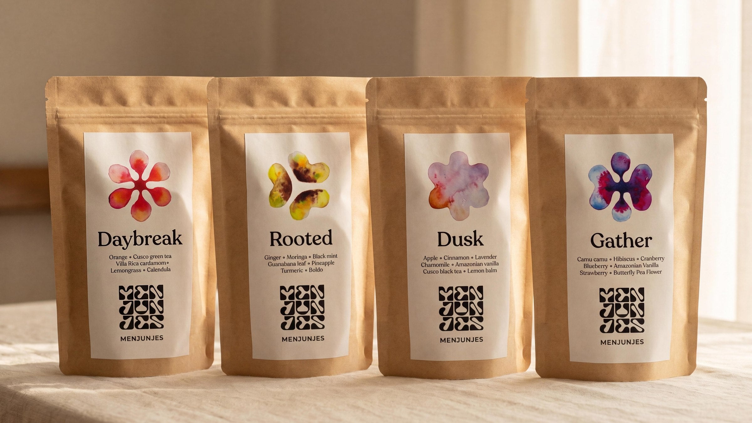 The four Menjunjes blends side by side on cream linen: Daybreak, Rooted, Dusk and Gather, each kraft pouch showing its watercolor mark and printed ingredient panel