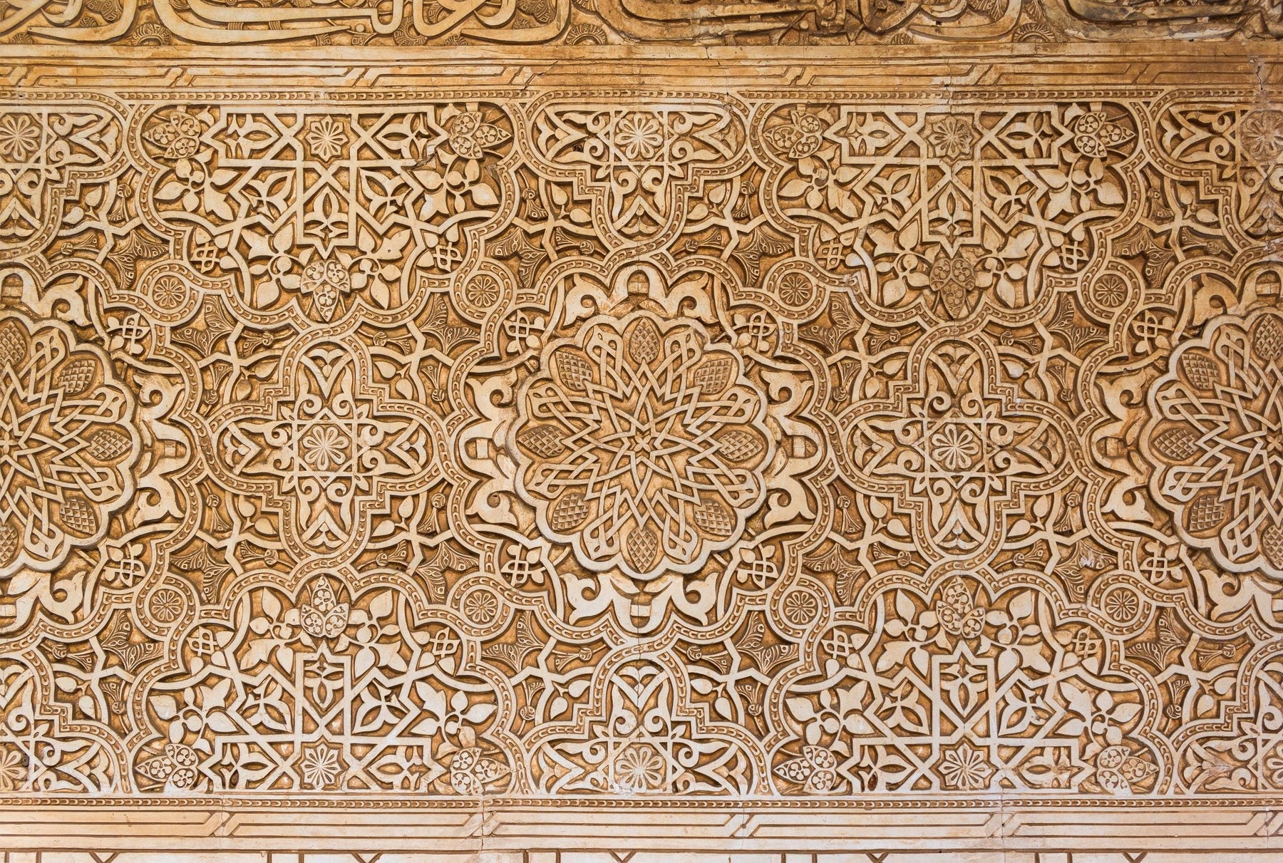 Carved arabesque at the Alhambra, toned dark: the visual opening of the word menjunje's thousand-year story