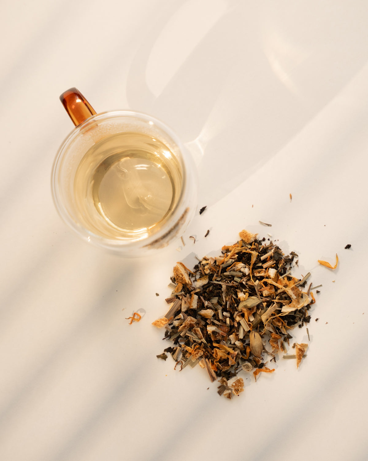 Daybreak brewed pale gold in a clear double-wall glass cup, beside the loose blend