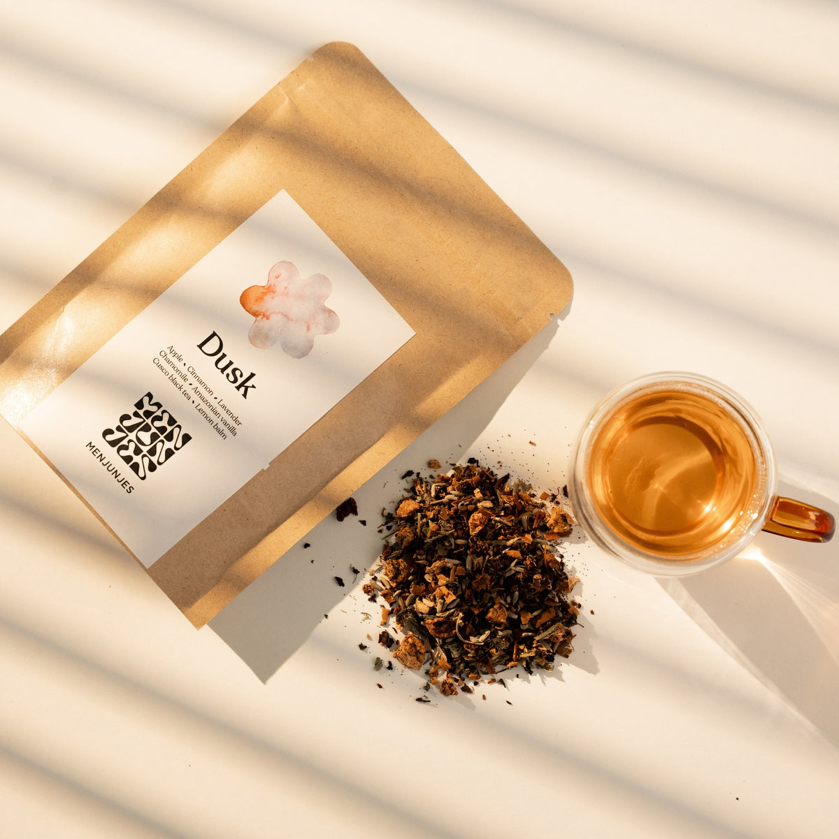 The Menjunjes Dusk pouch with a pile of the loose blend and a glass cup of the brewed tea