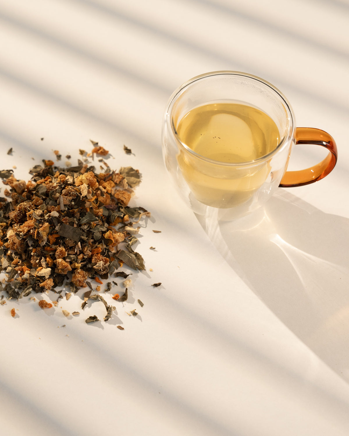 Rooted brewed in a clear double-wall glass cup beside the loose blend